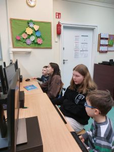 dzieci młodsze i starsze siedzą przed monitorami komputerów