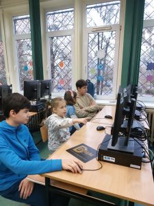 dzieci młodsze i starsze siedzą przed monitorami komputerów